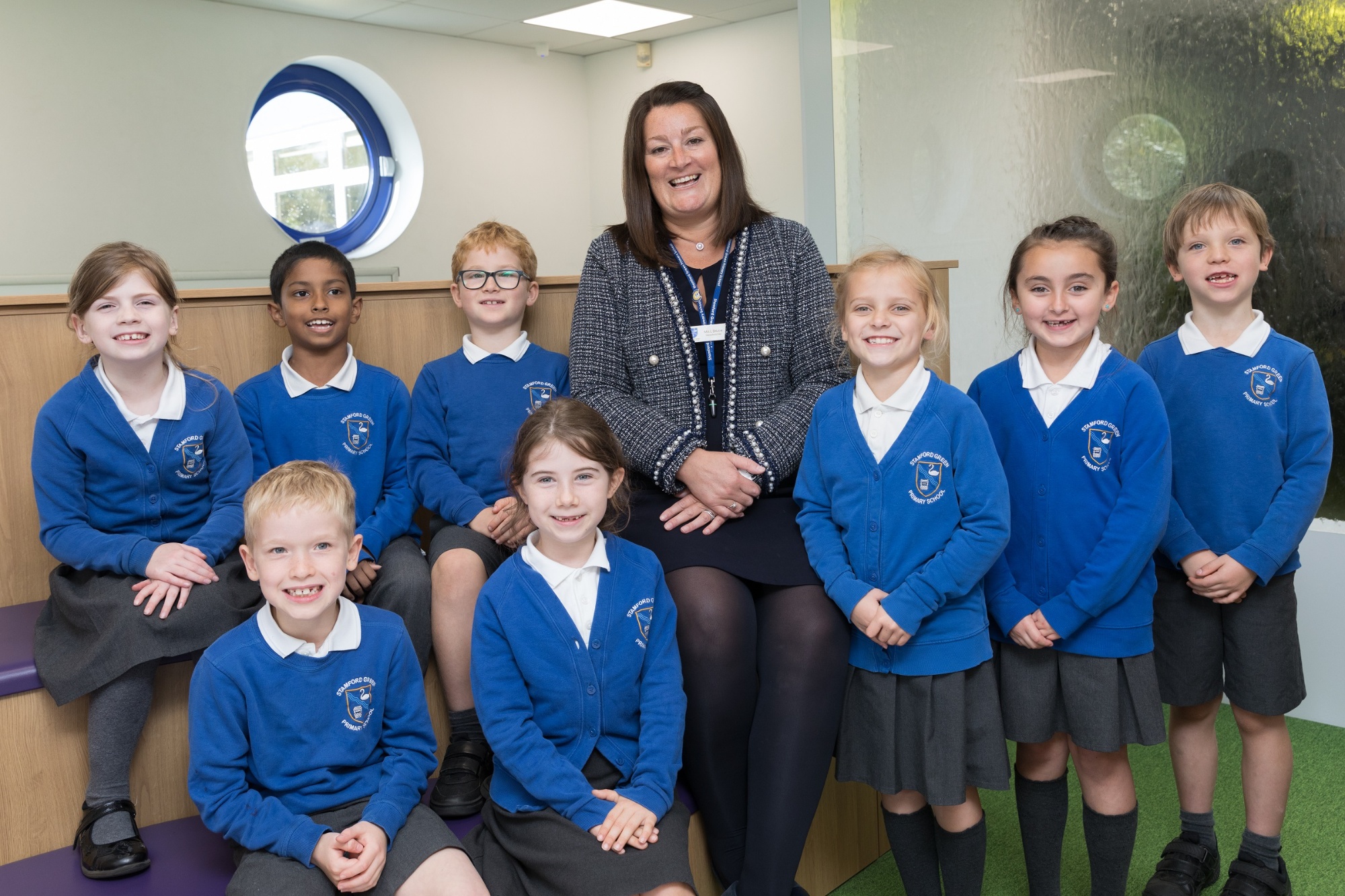 The head teacher standing in the library with a group of children.  They are all smiling.