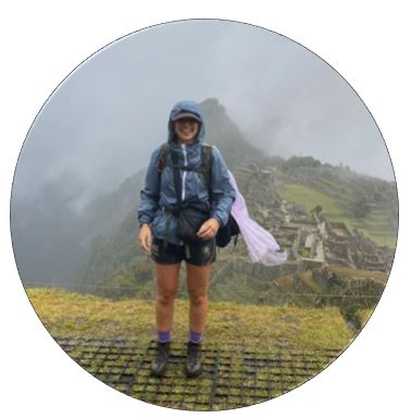 A ;ady stands on a mountainside wearing a raincoat
