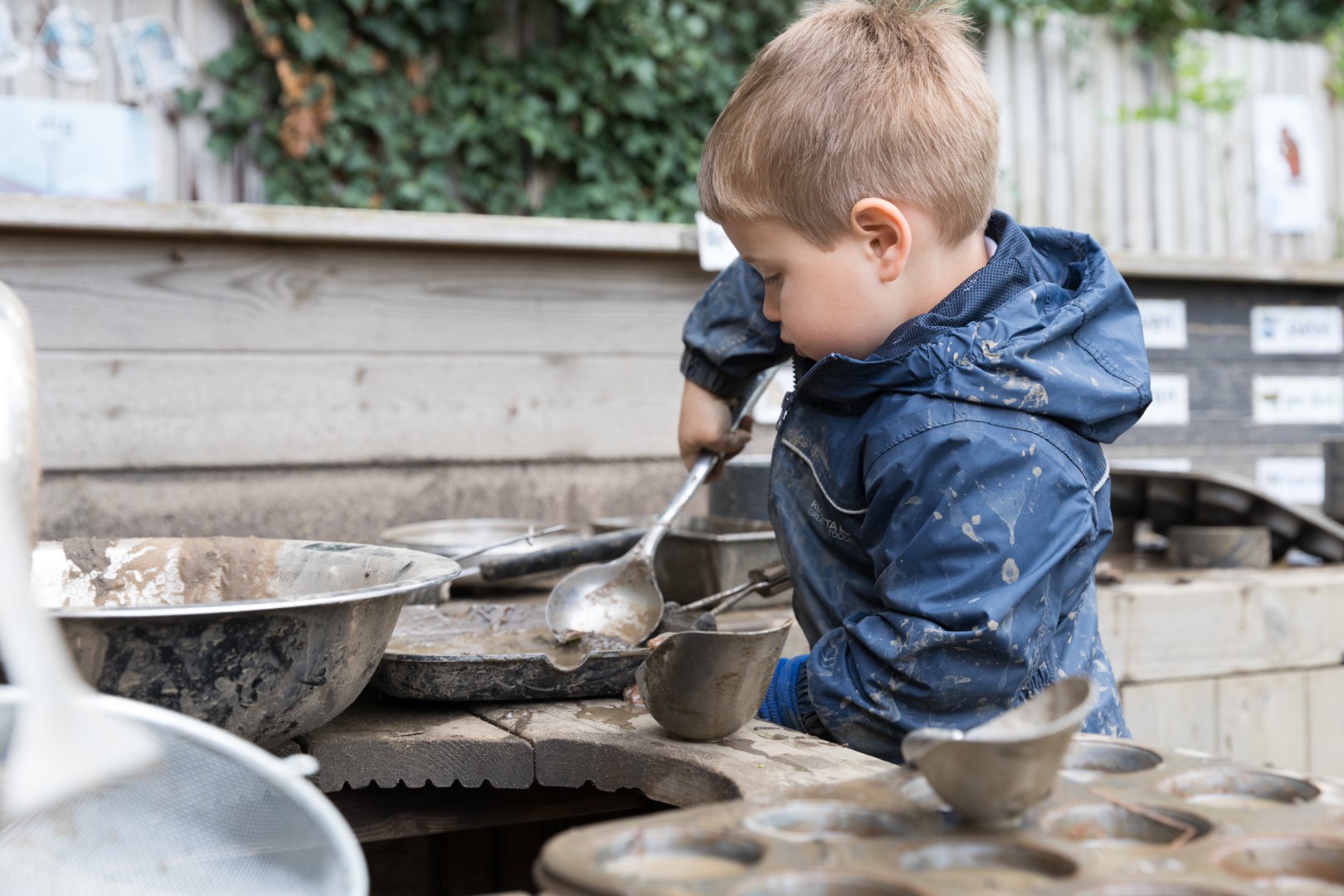 Boy in coat playing in mud kitchen